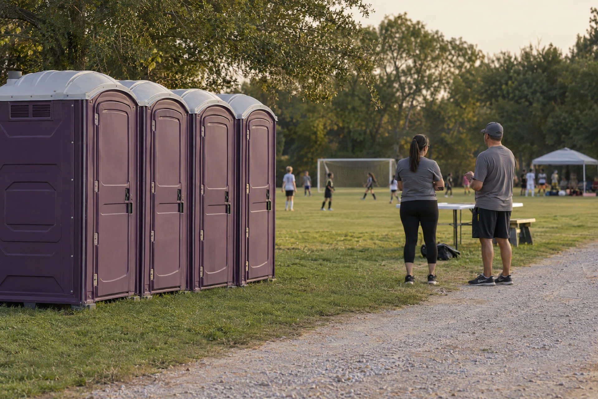 Portable restrooms beside a soccer field with event organizers nearby